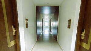 A long, narrow hallway with doors on both sides, leading to a bright room at the end. - Jewels Resorts (Jaipur)