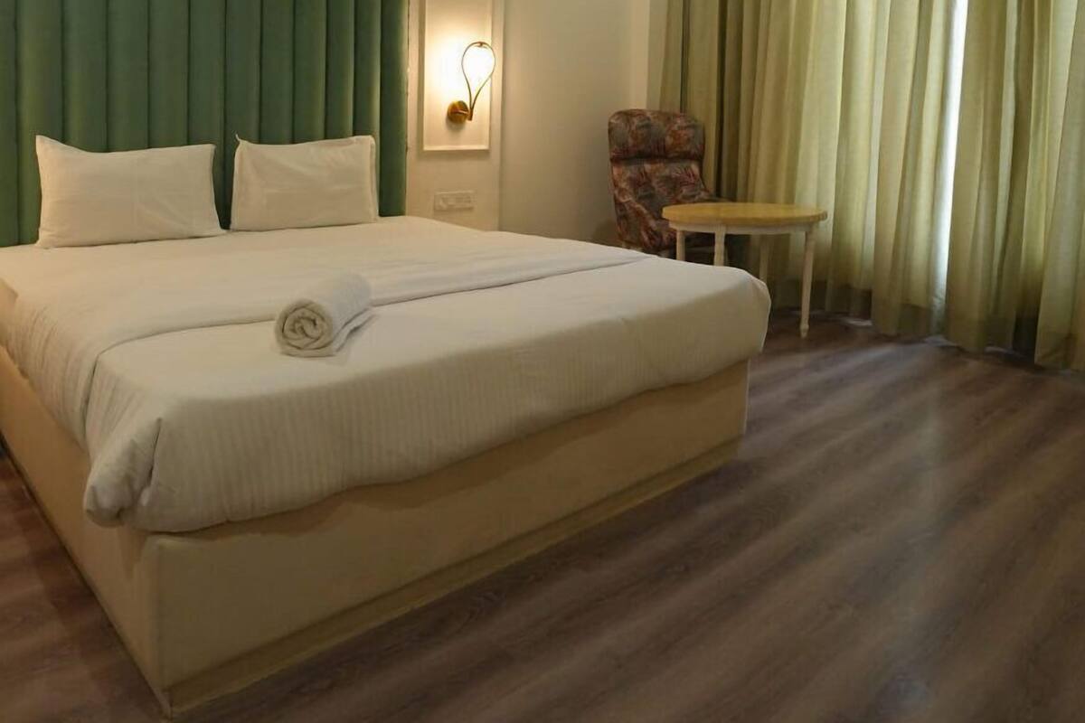 A hotel room with a large bed, a chair, a small table, and a wall-mounted light fixture.