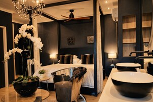 A modern hotel room with a bed, bedside lamps, a large mirror, a round table, and a chandelier.