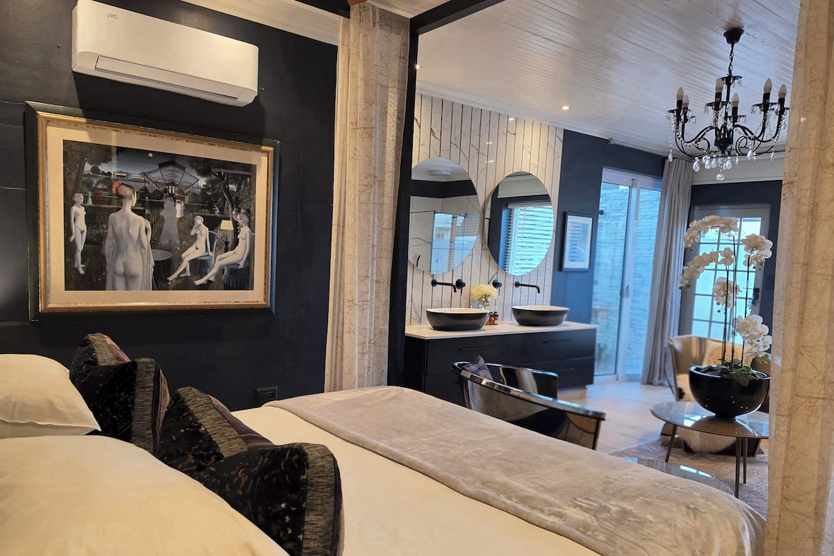 A modern hotel room with a large bed, a desk, a vanity with a mirror, and a chandelier.