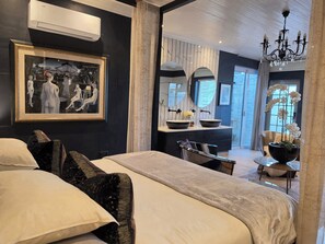 A modern hotel room with a large bed, a desk, a vanity with a mirror, and a chandelier. - Maison Pjure Boutique Hotel & Spa ( Adults Only ) (Montagu)