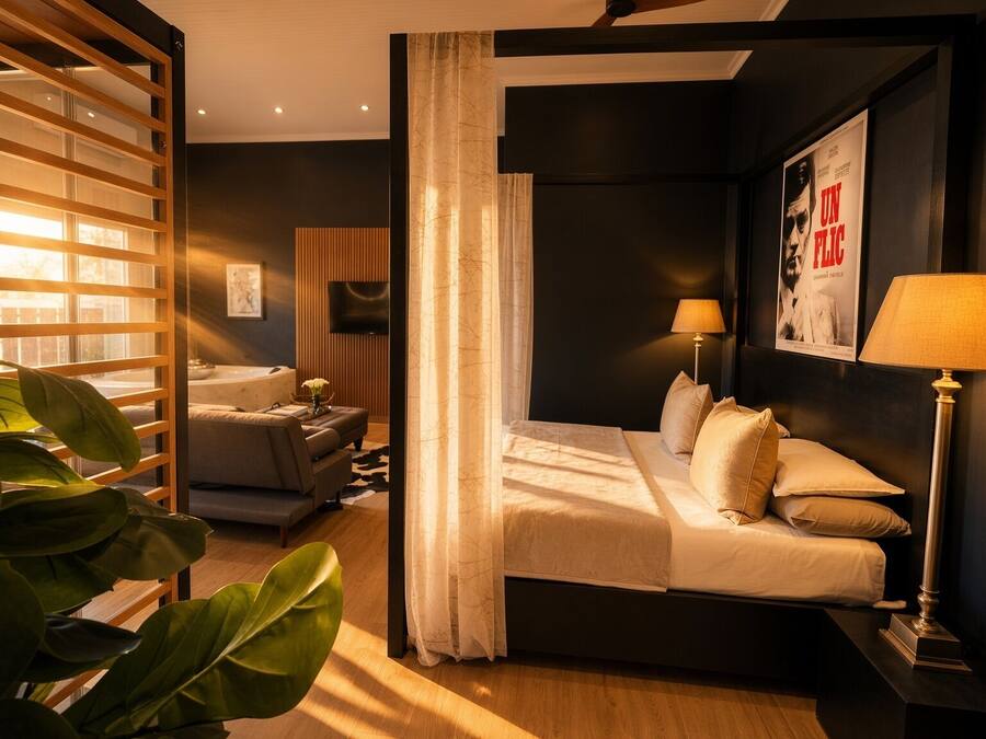 Moderni hotellihuone, jossa on sänky, yöpöytävalaisimet, televisio ja suuri ikkuna, jossa on sälekaihtimet.