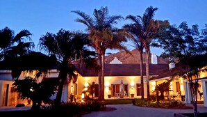 A resort with a well-lit entrance, palm trees, and a covered outdoor seating area. - Maison Pjure Boutique Hotel & Spa ( Adults Only ) (Montagu)