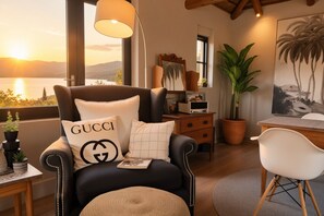 A modern living room with a leather armchair, a table with a lamp, a potted plant, and a painting of palm trees. - Maison Pjure Boutique Hotel & Spa ( Adults Only ) (Montagu)
