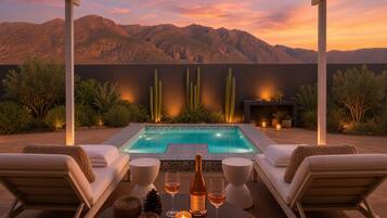 A pool area with lounge chairs, a table with drinks, and a view of mountains.