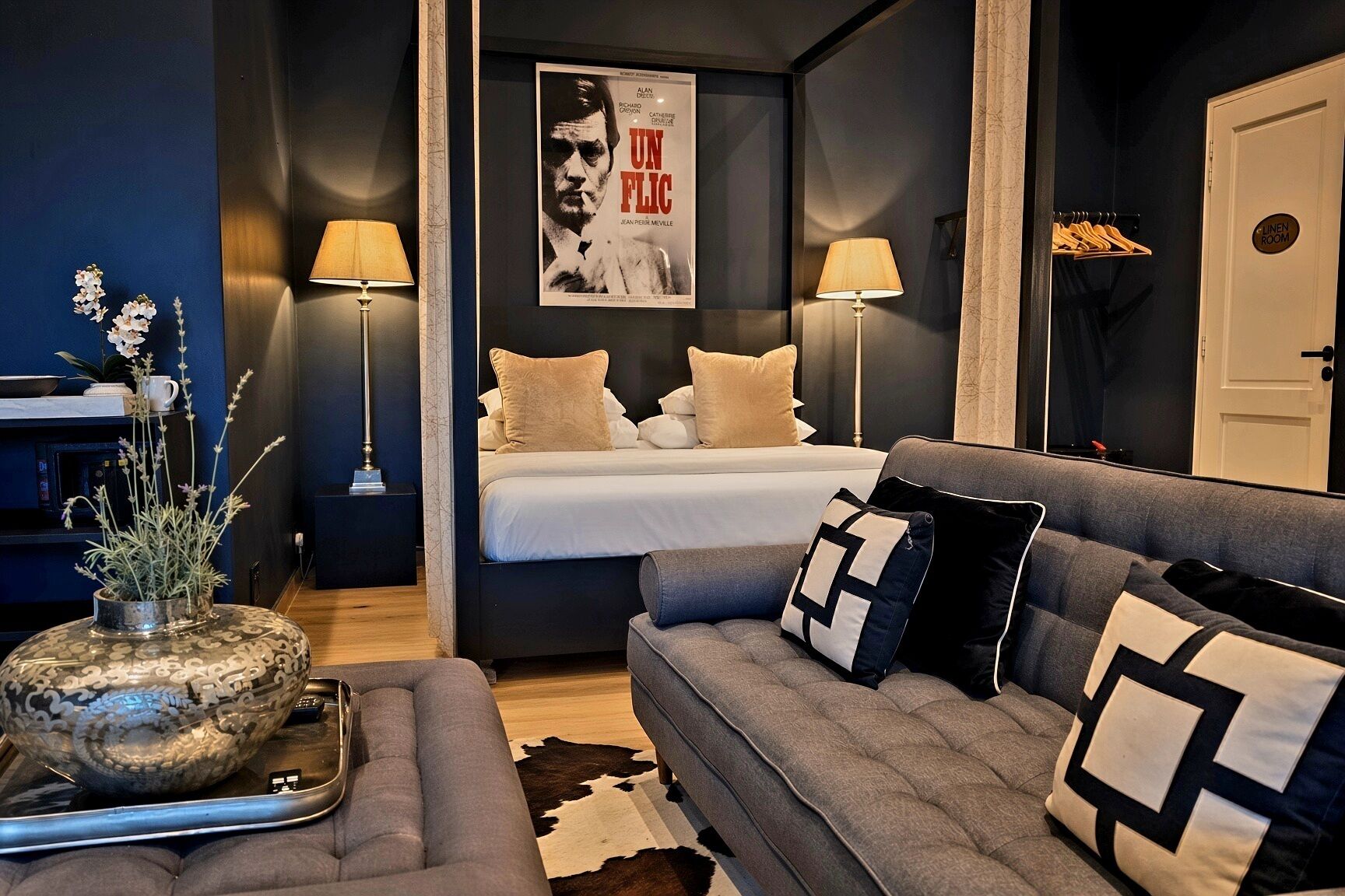 A modern bedroom with a bed, bedside lamps, a grey sofa, and a poster on the wall.
