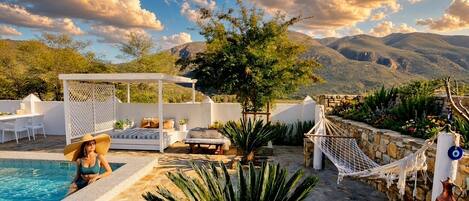 Zona junto a la piscina con asientos, una hamaca y vistas a las montañas.