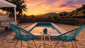 Zona de piscina con dos sillas y una mesa, rodeada de muros de piedra y vistas a las montañas.