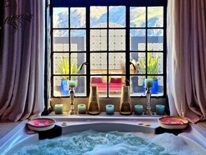 A spa area with a bathtub, candles, and a window with a view of a garden. - Maison Pjure Boutique Hotel & Spa ( Adults Only ) (Montagu)