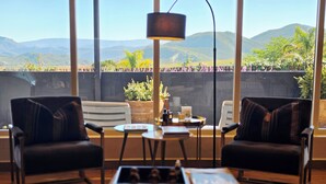 A room with two leather chairs, a small table, a floor lamp, and a view of mountains through large windows. - Maison Pjure Boutique Hotel & Spa ( Adults Only ) (Montagu)