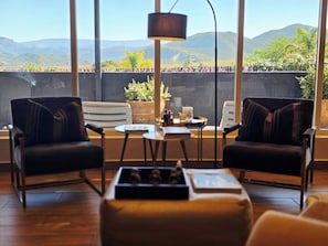 A room with two leather chairs, a small table, a floor lamp, and a view of mountains through large windows. - Maison Pjure Boutique Hotel & Spa ( Adults Only ) (Montagu)
