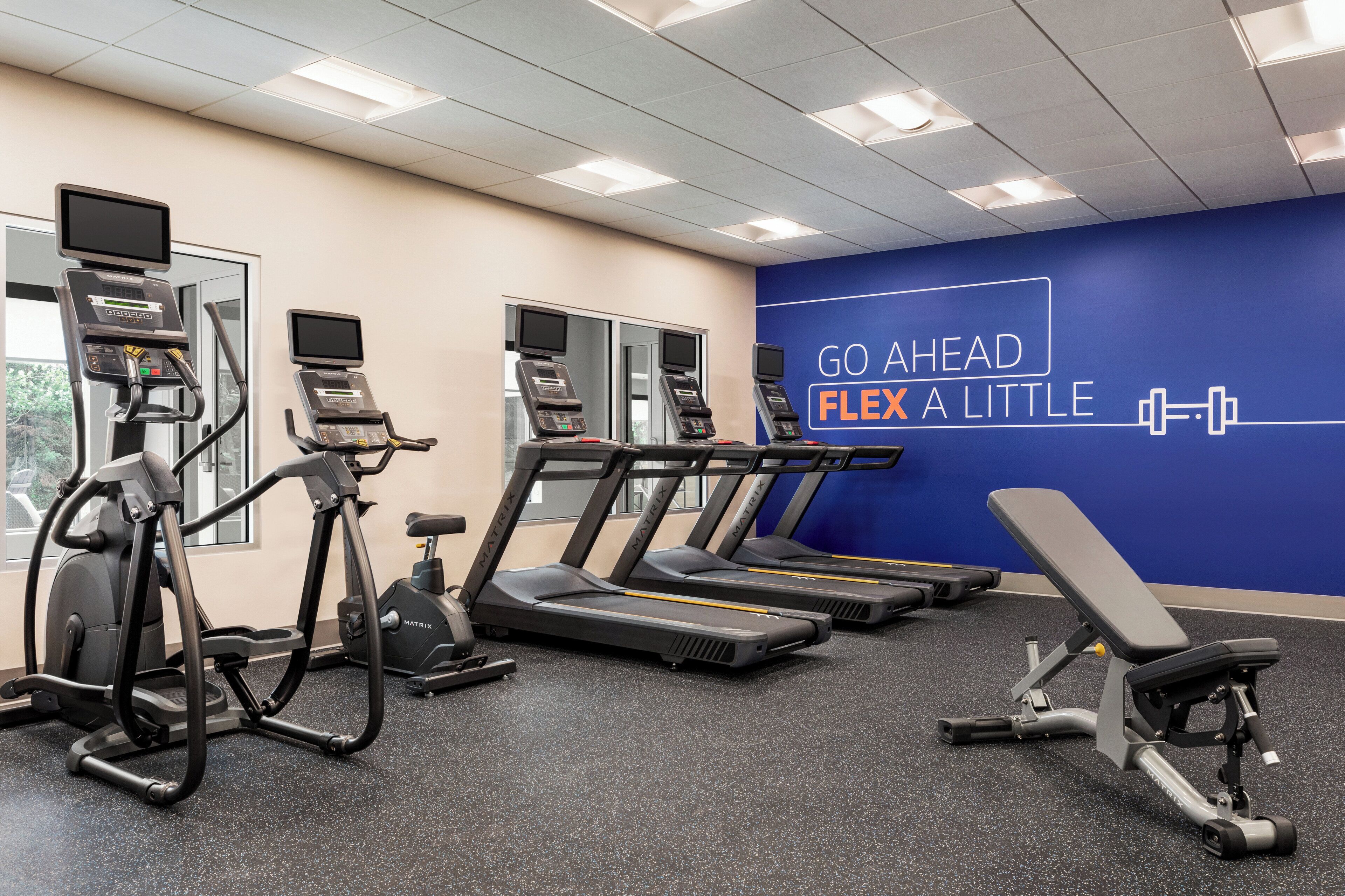 A gym with treadmills, elliptical machines, and a bench.