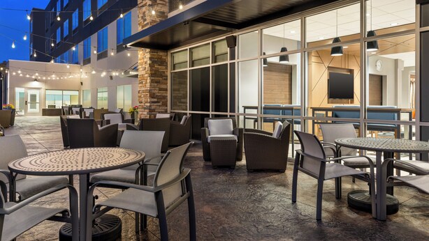 An outdoor patio area with round tables and chairs, large windows, and string lights. - Holiday Inn Express and Suites Rhinelander by IHG (Rhinelander)