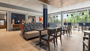 A modern cafe with wooden tables and chairs, a counter with coffee machines, and large windows offering a view of greenery. - Holiday Inn Express and Suites Rhinelander by IHG (Rhinelander)