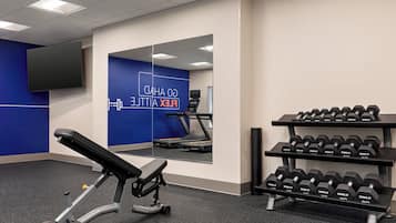 Un gimnasio con banco de pesas, mancuernas, cinta de correr y un espejo.