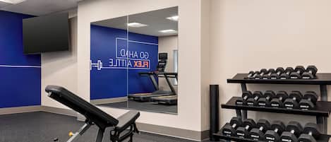 A gym with a bench press, dumbbells, a treadmill, and a mirror.