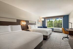 Hotellihuone, jossa on kaksi sänkyä, työpöytä, tuoli, ikkuna, josta on näkymä puille, ja seinään kiinnitetty valaisin.