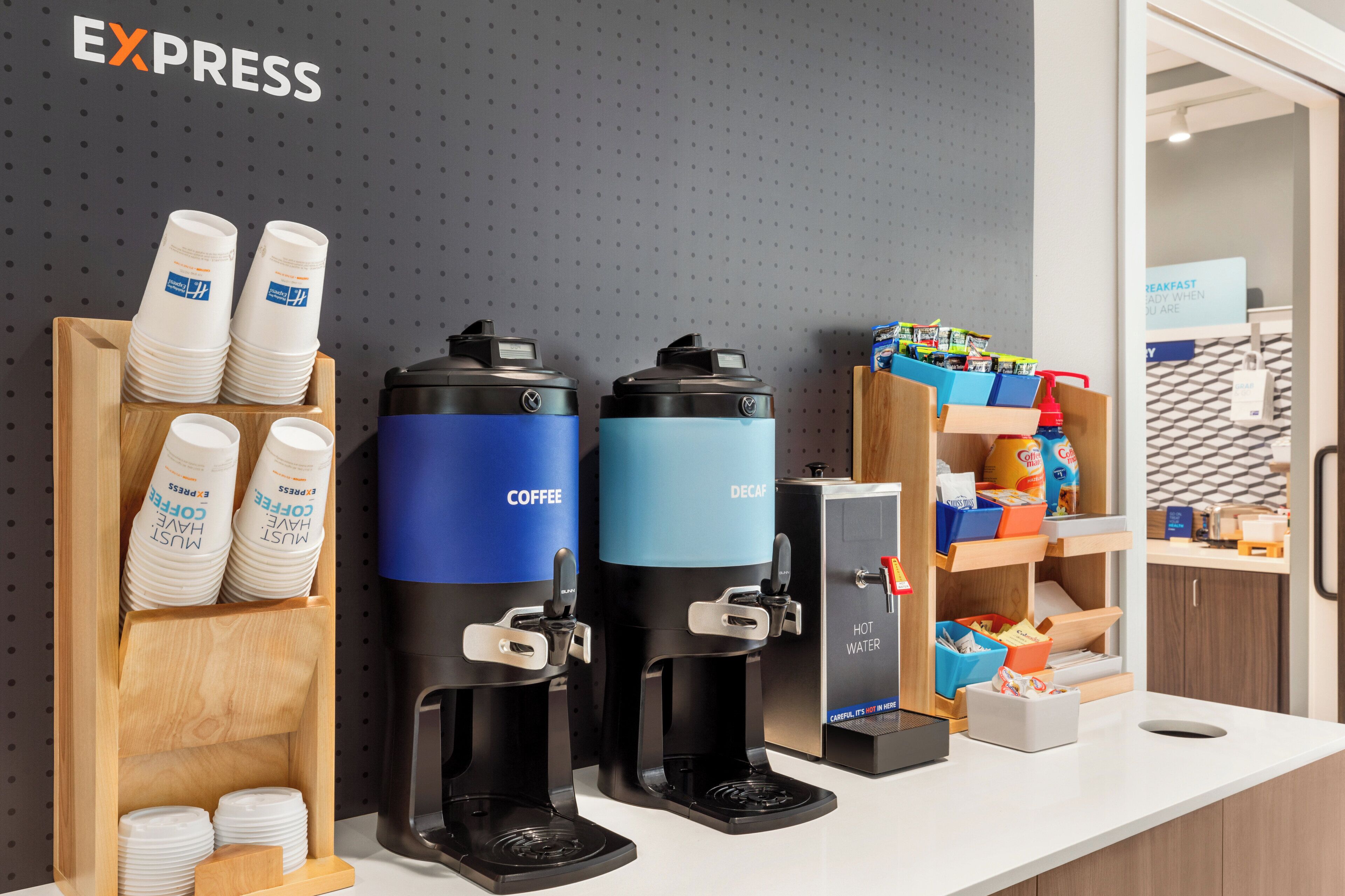 Een koffiehoek met twee koffieautomaten, een heetwaterdispenser en een bekerhouder met wegwerpbekers.
