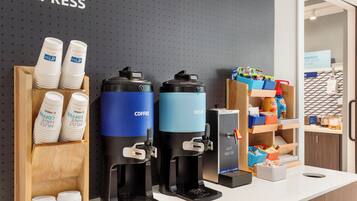 Een koffiehoek met twee koffieautomaten, een heetwaterdispenser en een bekerhouder met wegwerpbekers.
