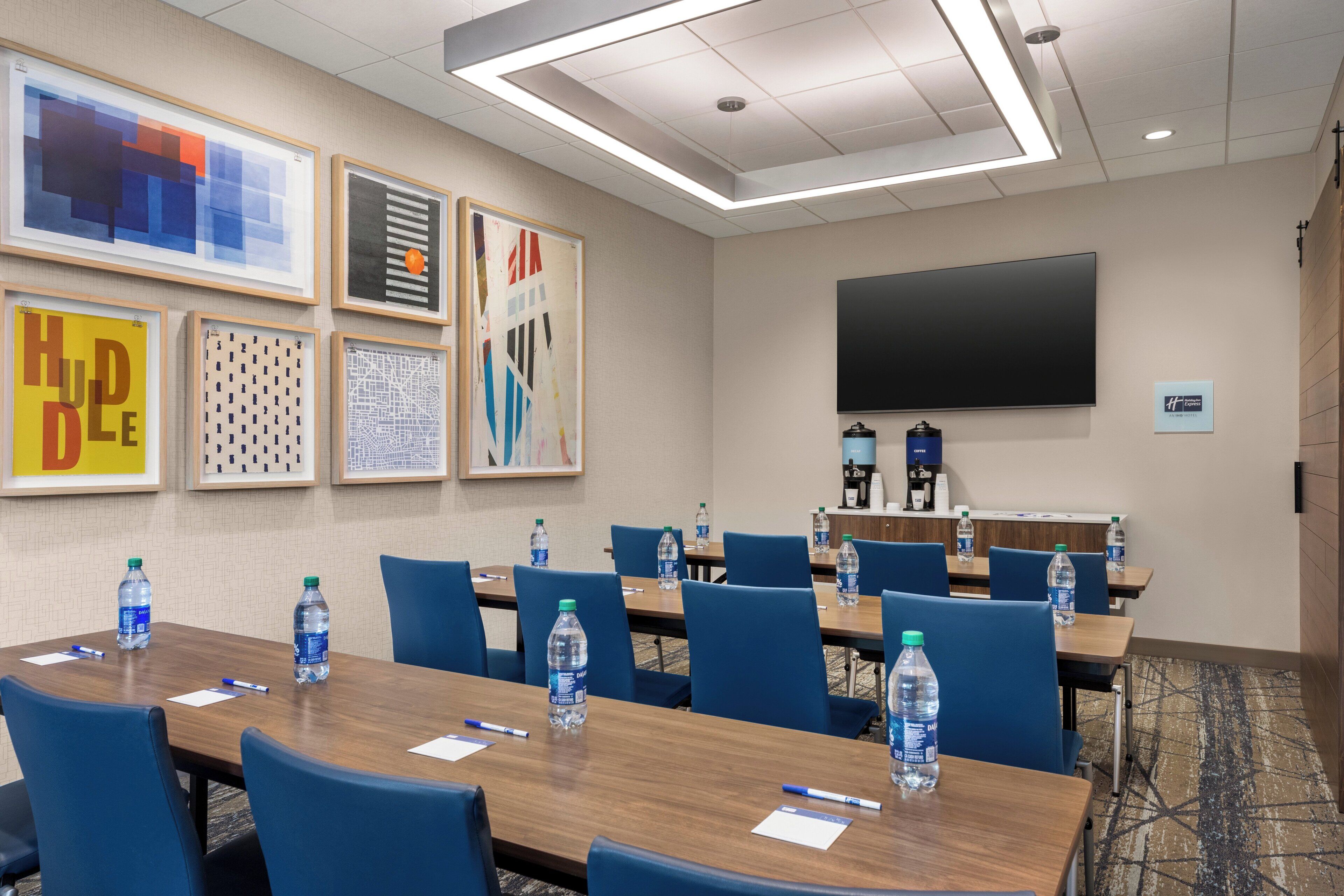A conference room with a long table, blue chairs, water bottles, and framed artwork on the walls.