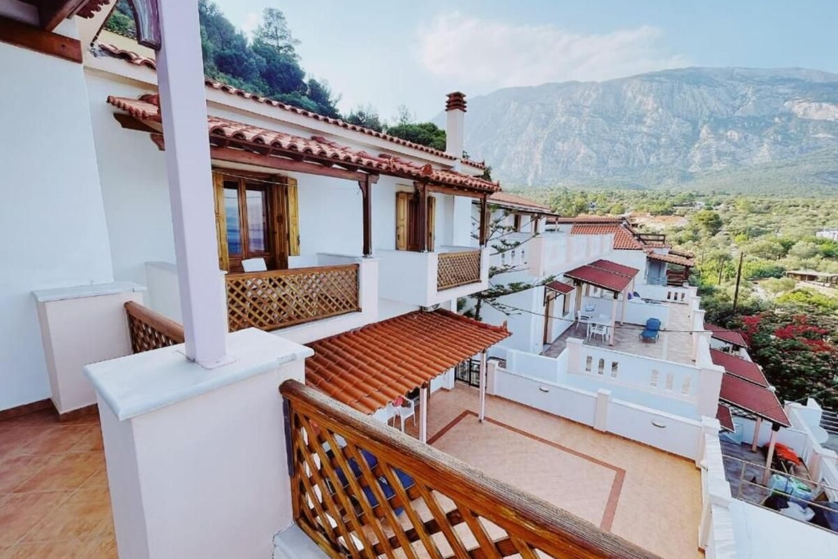 Un edificio residencial con balcón, cerca de madera y vista a un paisaje montañoso.