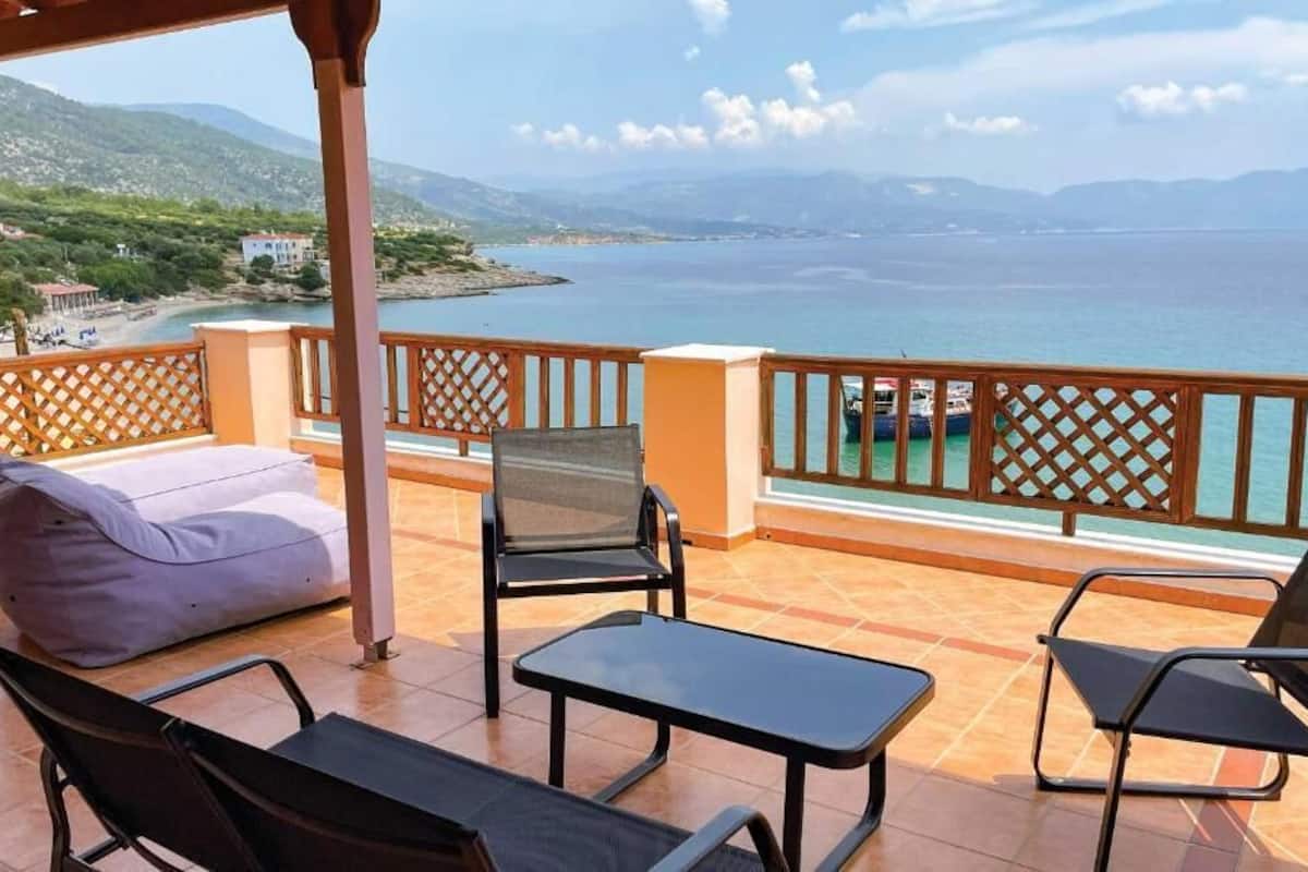 A terrace with outdoor furniture, a view of the sea, and a distant landscape.