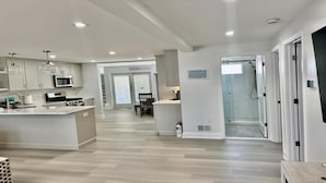Uma cozinha moderna com uma ilha central, uma área de refeições com uma cadeira e um espaço de chuveiro com padrão de tijolos em herringbone.