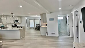 Une cuisine moderne dotée d’un îlot central, d’un coin repas avec une chaise et d’un espace douche avec un motif de carrelage en chevrons.