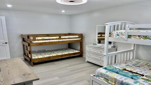 Un lit superposé pour enfants, avec une commode et un miroir, une table en bois et une couvre-lit à motifs.