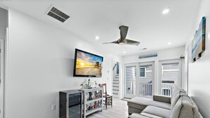Uma sala de estar moderna com televisão de tela plana, ventilador de teto, sofá e mesa de centro.