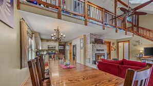A spacious dining area with a wooden table and chairs, a chandelier, and a stone fireplace.