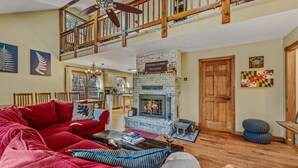 A spacious living room with a fireplace, a red sofa, a dining area, and a wooden staircase.