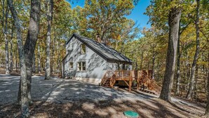 A cabin with a wooden deck and stairs leading to a porch, surrounded by trees.
