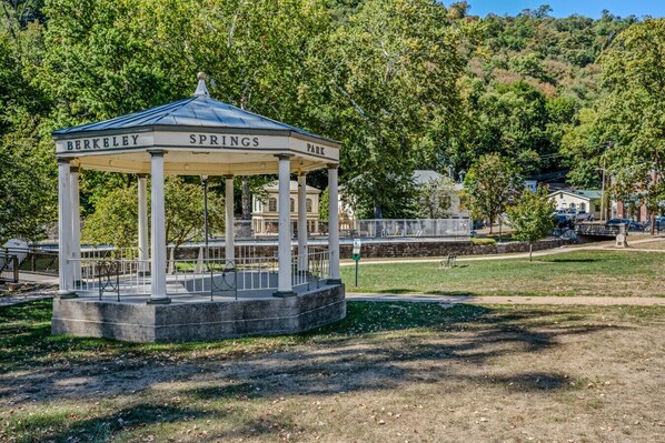 Un pabellón con la inscripción "BERKELEY SPRINGS PARK" en su techo, rodeado de árboles y una zona cubierta de césped.
