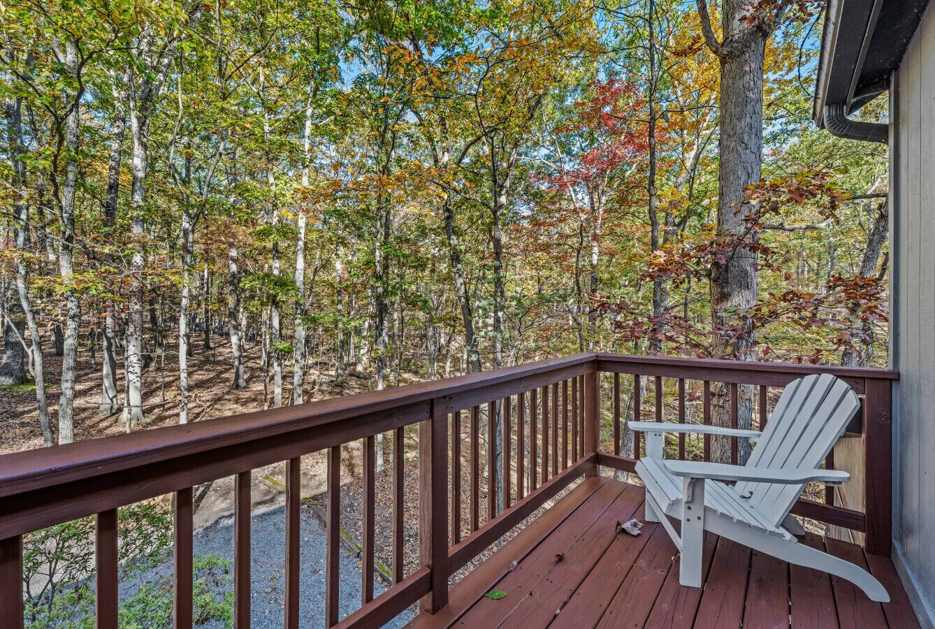 Une terrasse en bois avec un fauteuil Adirondack blanc, entourée d’arbres aux feuilles d’automne.