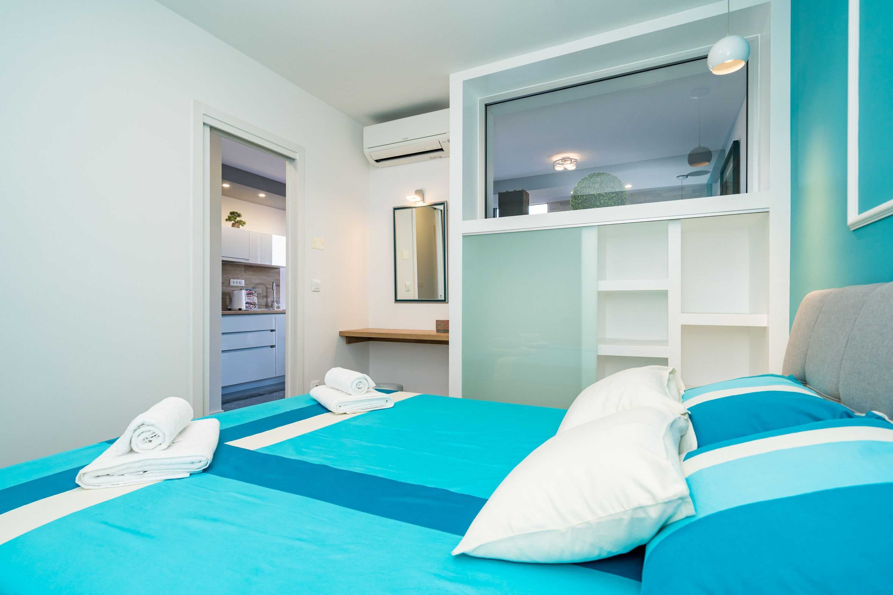 Une chambre d’hôtel avec un lit, une fenêtre, un miroir et une salle de bain visible à travers une porte ouverte.