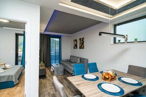 A modern room with a dining table set for four, a sofa, and a small window with plants. - Apartments Villa Arcadia (Dubrovnik)