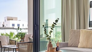 A modern living room with a sofa, chairs, a glass table, and a view of buildings through large windows. - Sanders Evolution 2 Lovely 2 Bedroom Apartment With Balcony (Limassol)