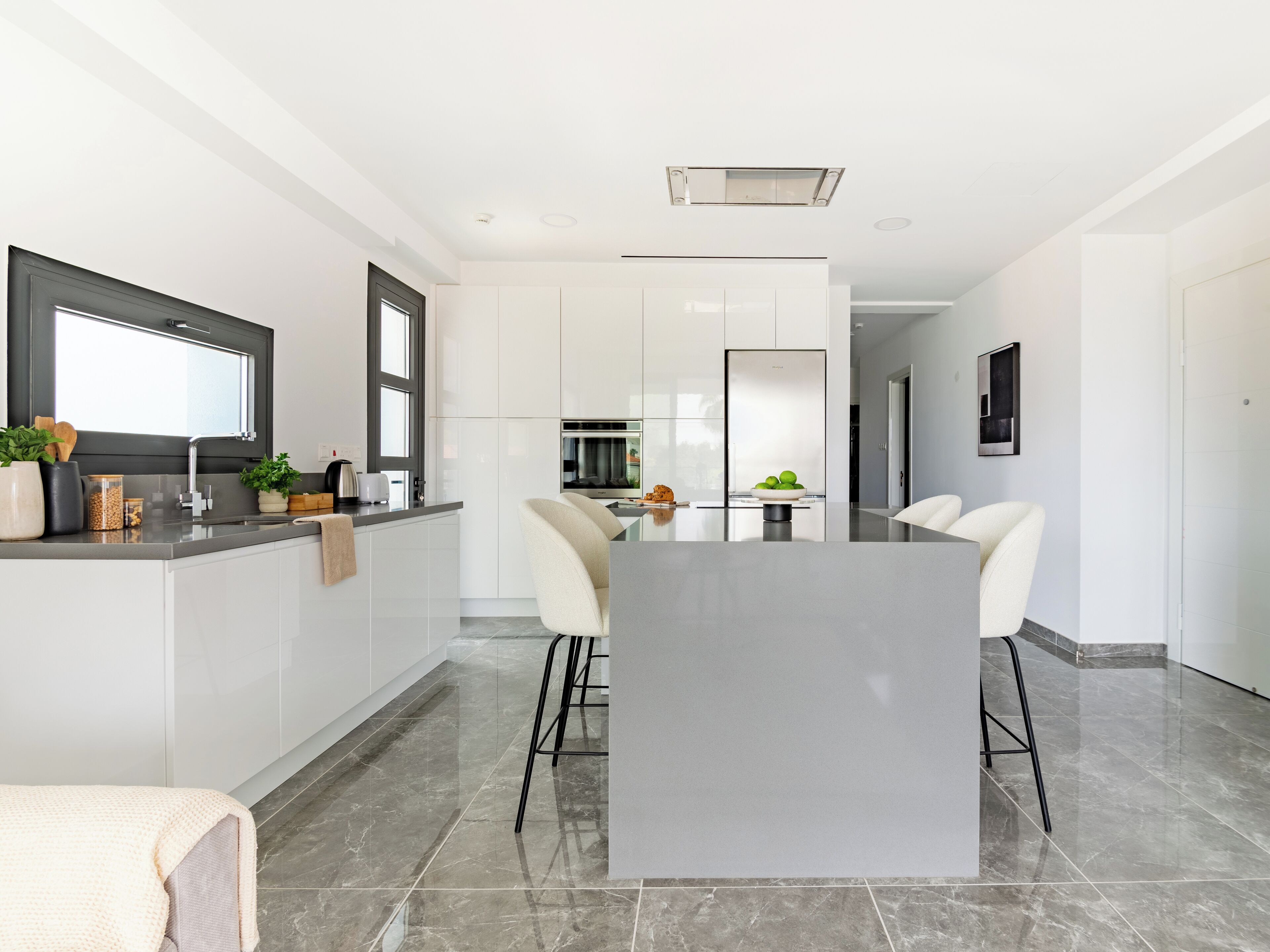 A modern kitchen with white cabinets, a central island, and a dining area with a table and chairs.