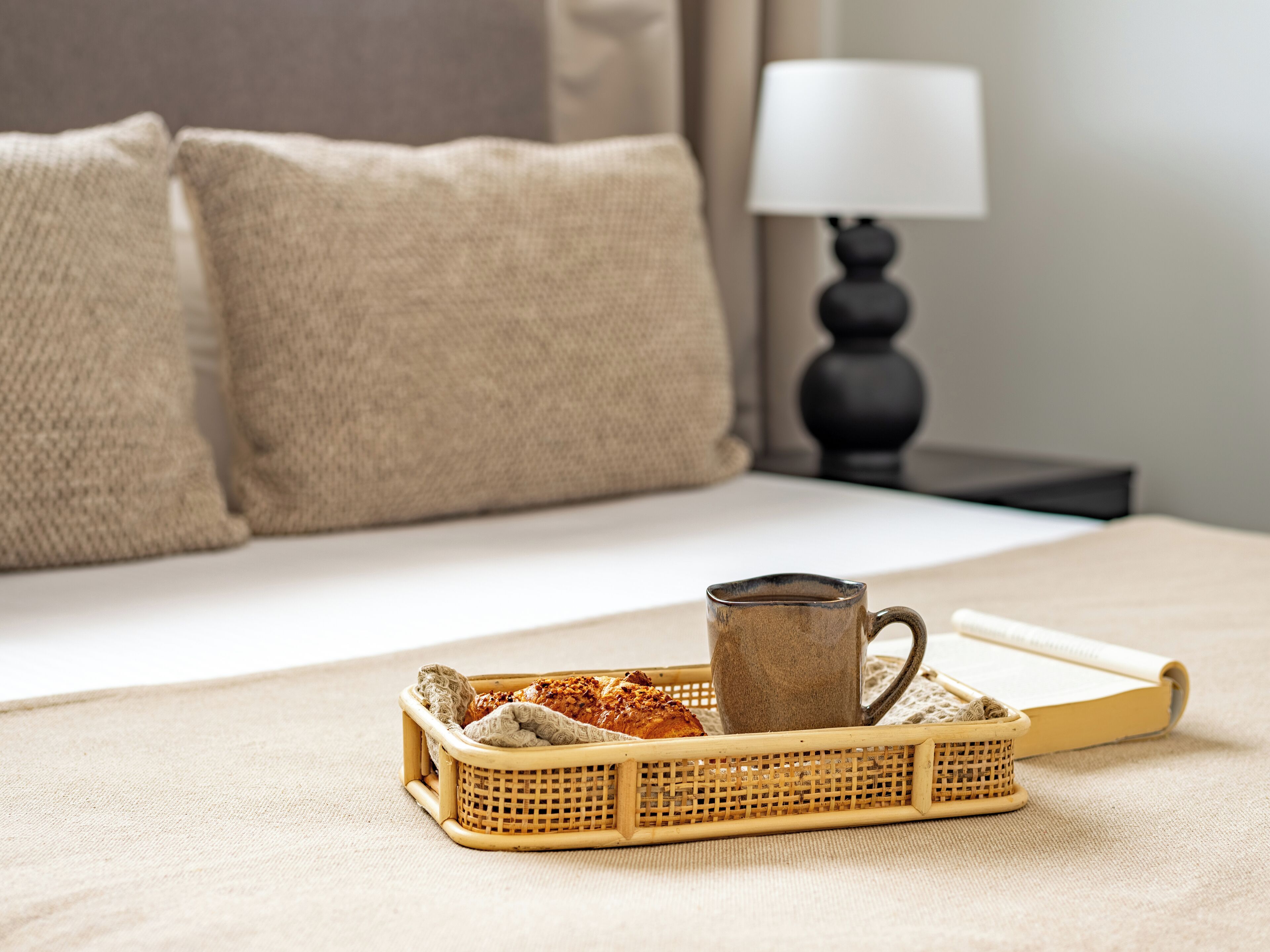 Cama bem arrumada com uma bandeja de pão e uma caneca sobre um edredom texturizado.