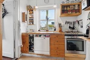 A kitchen with wooden cabinets, a dishwasher, an oven, and a window with a view of the outside. - Cozy old cottage in Asaa (Asaa)