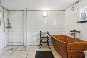 A bathroom with a wooden bathtub, a shower, and a shelf with toiletries.