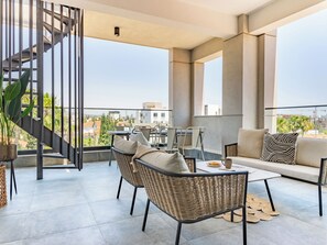 A modern outdoor balcony with wicker furniture, a staircase, and a view of the cityscape. - Sanders Evolution 2 - 2 Bedroom Apartment With Private Rooftop and Jacuzzi (Limassol)