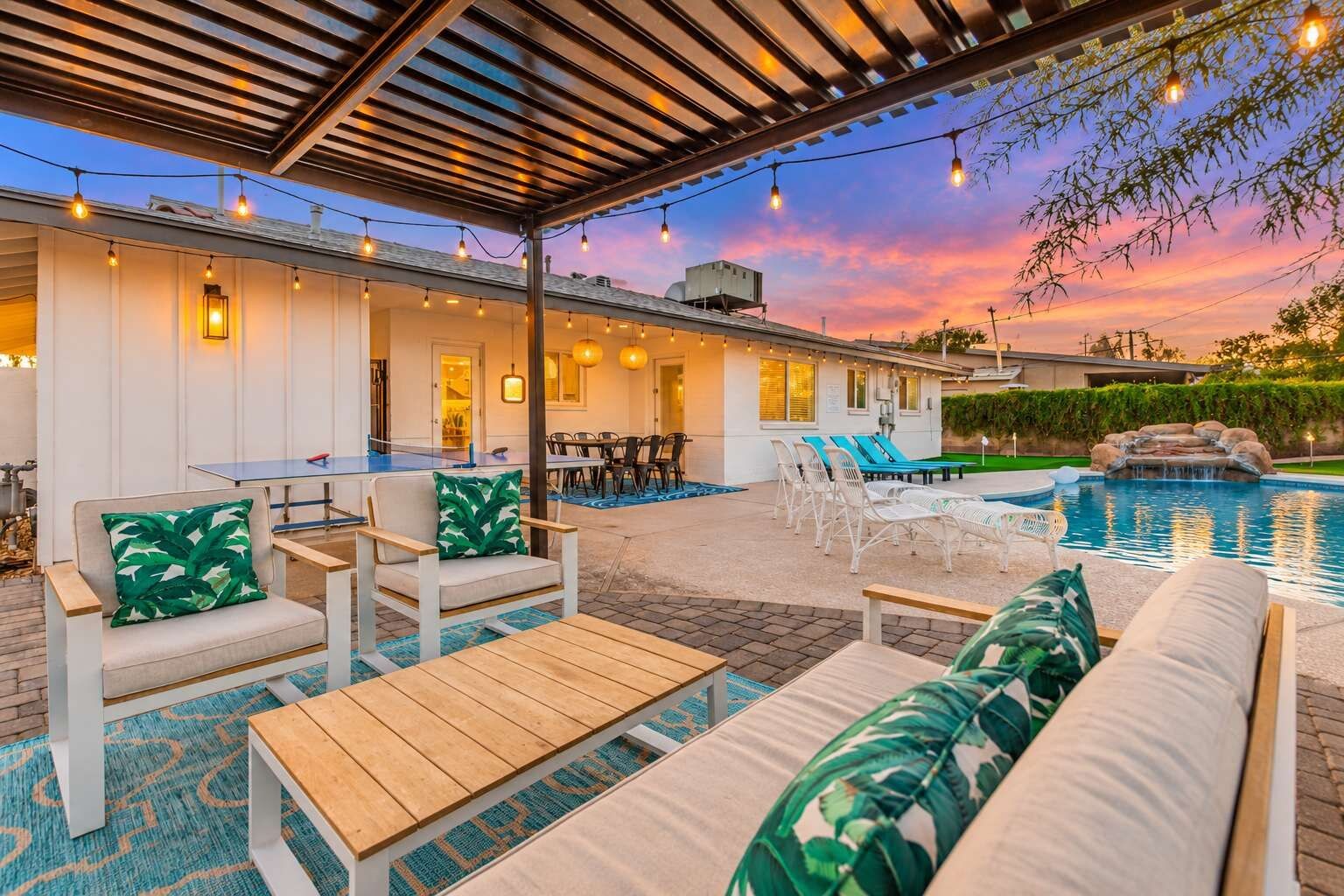An outdoor patio area with a pool, seating, and string lights.