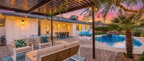 An outdoor pool area with a covered seating area, lounge chairs, and a wooden bench.