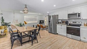 Eine moderne Küche mit weißen Schränken, Edelstahlgeräten und einem Essbereich mit Holztisch und Stühlen.