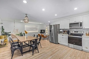 A modern kitchen with white cabinets, stainless steel appliances, and a dining area with a wooden table and chairs.
