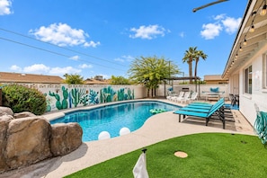 A swimming pool with a cactus mural, lounge chairs, and a grassy area. - Vacay on Villa | Old Town |Swim, Putt, Play & Stay (Scottsdale)