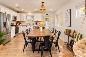 A modern kitchen with white cabinets, a stainless steel refrigerator, a wooden dining table, and black chairs.