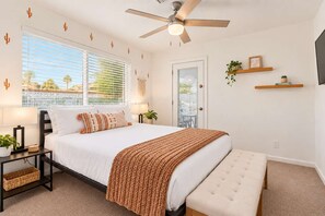 A bedroom with a bed, bedside tables, a ceiling fan, a bench, and a view through a door. - Vacay on Villa | Old Town |Swim, Putt, Play & Stay (Scottsdale)